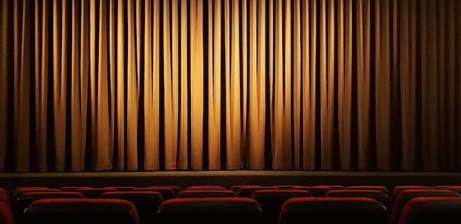 Some rows of seats in a movie theater, with a stage in front, and the curtains drawn